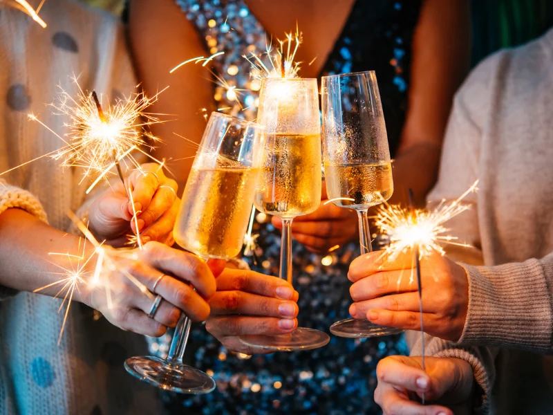 Pessoas celebrando com taças de espumante e velas de faíscas acesas, criando um clima alegre e brilhante.