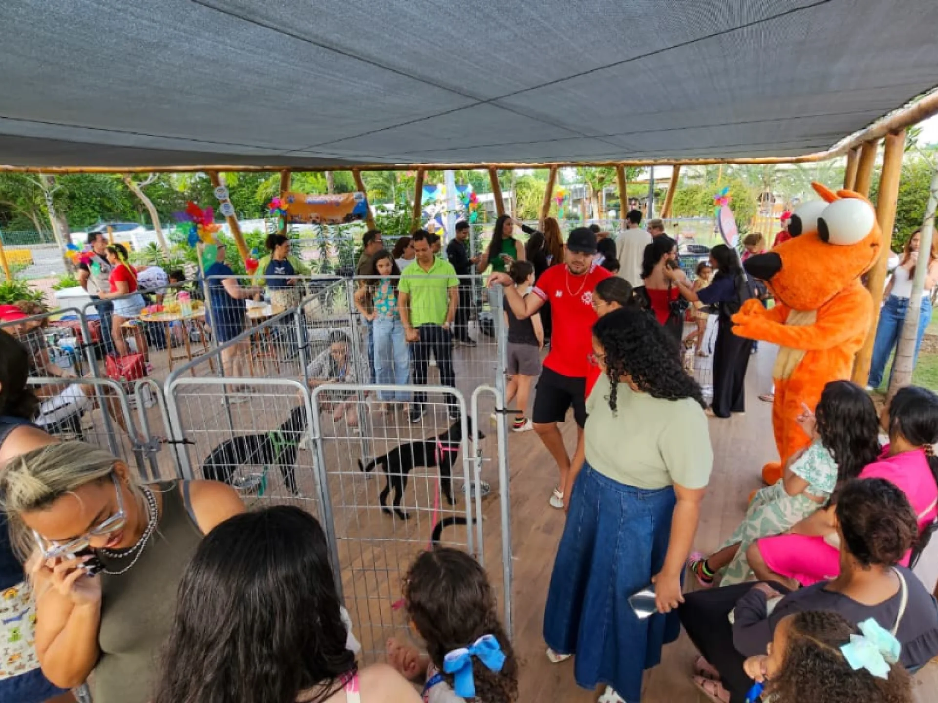 Multidão reunida em evento de adoção no PETMAR, com cães em cercados e um mascote laranja interagindo com o público