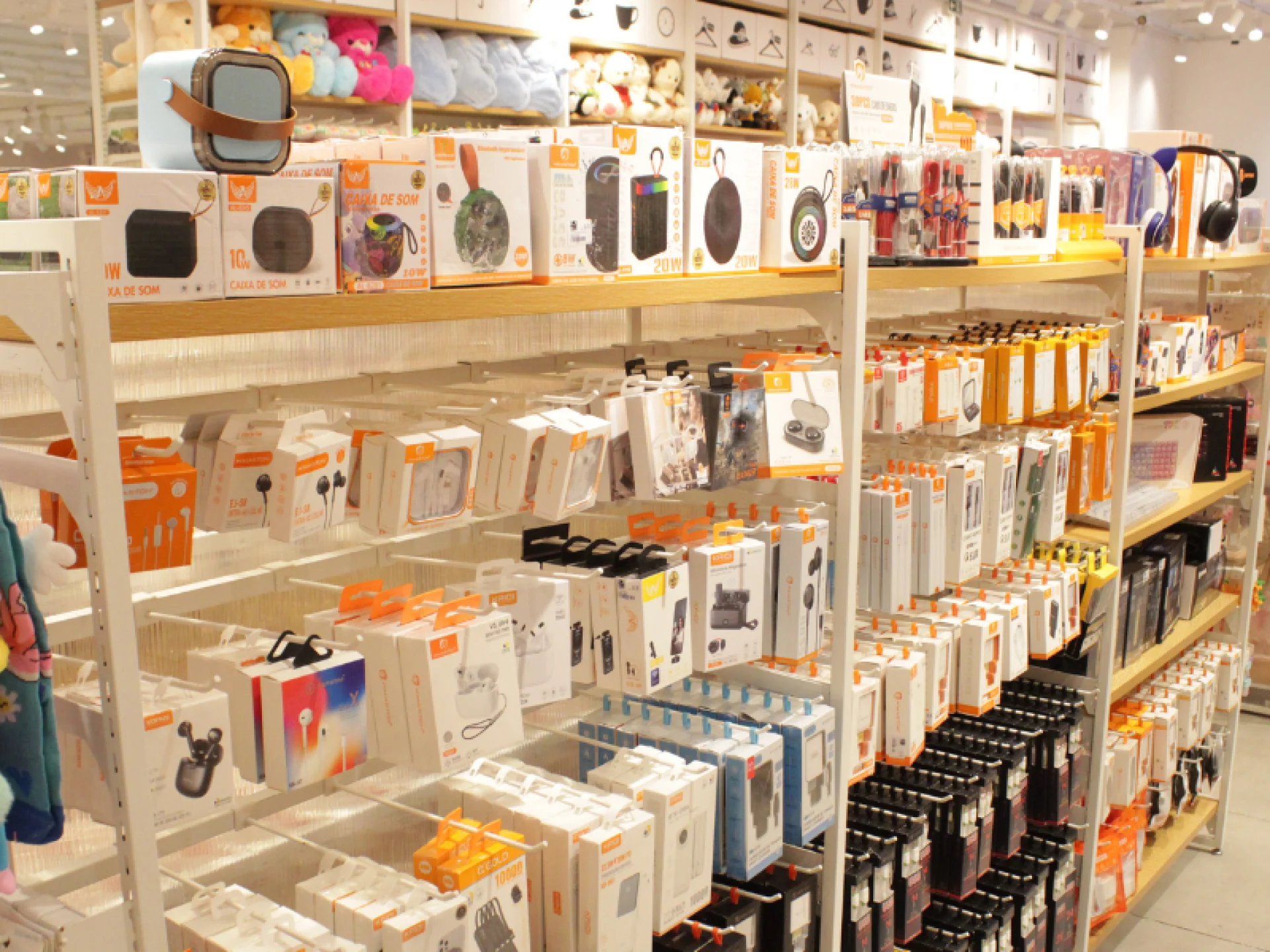 Vista ampla de uma loja com prateleiras brancas e de madeira repletas de diversas caixas de eletrônicos e acessórios, como fones de ouvido e caixas de som.