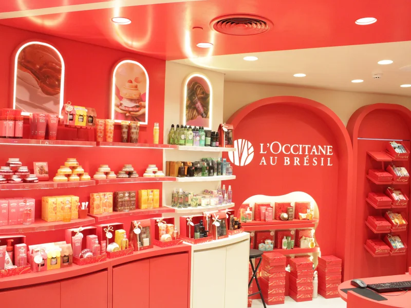 Vista de uma loja L'Occitane au Brésil, destacando prateleiras repletas de produtos e embalagens vermelhas, em um ambiente predominantemente vermelho e branco.