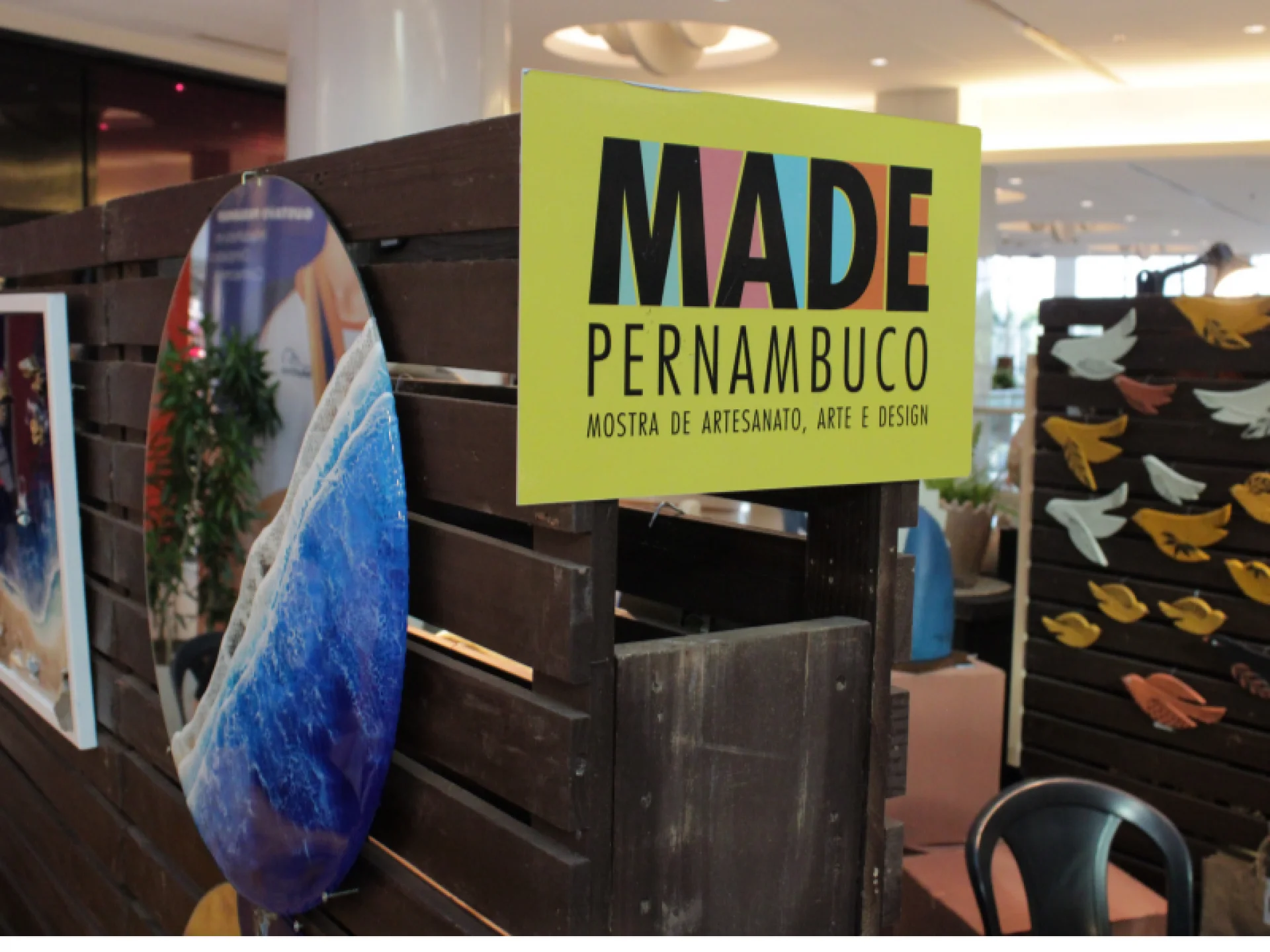 A imagem mostra uma placa da feira MADE PERNAMBUCO em frente a um estande de madeira rústica. A imagem mostra uma placa da feira MADE PERNAMBUCO em frente a um estande de madeira rústica.