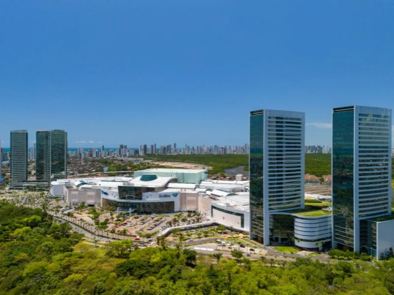 A imagem mostra o RioMar Recife de uma vista aérea com as cinco torres empresariais e o manguezal em volta.