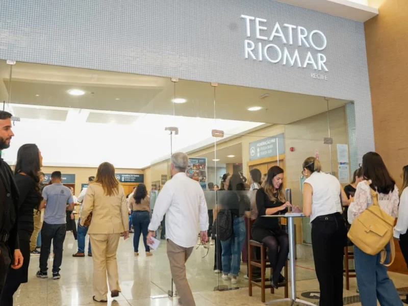 Entrada do Teatro RioMar Recife, com pessoas chegando e sendo recepcionadas em balcões de credenciamento.